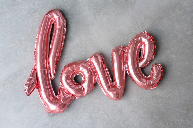 Love word from pink inflatable balloon on grey concrete background. The concept of romance, Valentine's Day. Love rose gold foil balloon