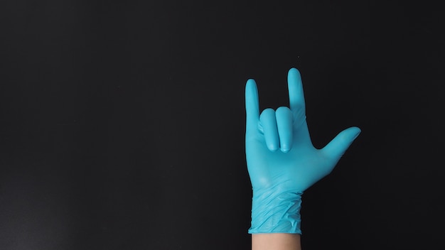 The love-you gesture or I love you hand sign with hand wearing blue glove on black background.