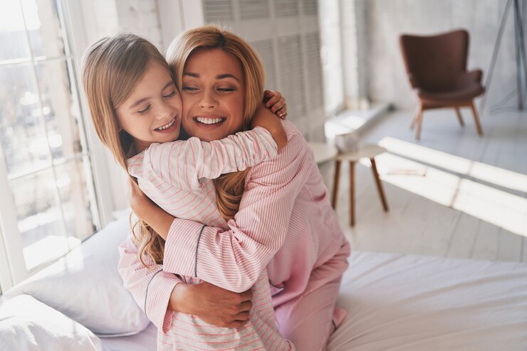 Photo love you so much! top view of cute little girl embracing her mother while sitting on the bed at home