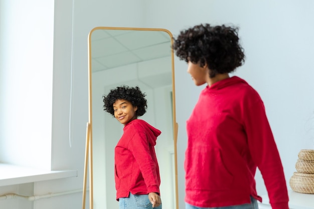 Foto ama te stesso, bella giovane donna afroamericana sorridente che balla godendosi il suo riflesso allo specchio