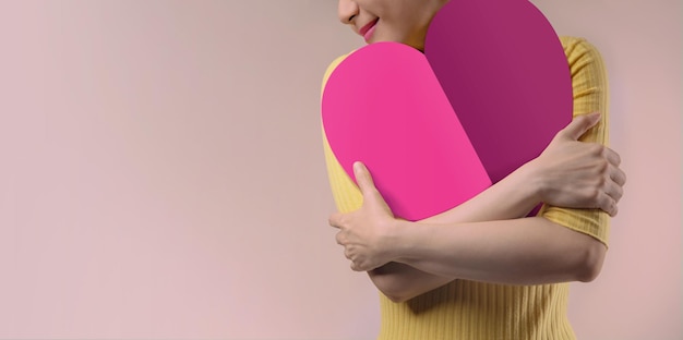 Love Yourself Concept. Smiling Female Embracing and Hugging Herself and Pink Heart Shape paper.  Positive Mind. Wellbeing Mental Health. Single in Valentines Day