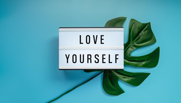 Photo love yourself quote with tropical monstera on blue background