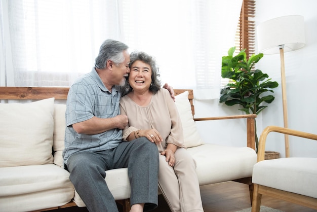 Lovegrey-haired Aziatische man knuffelen zijn vrouw met tederheid zitten op de bank thuis
