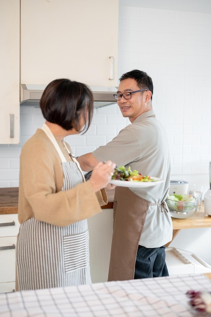 素敵なアジア人夫婦がキッチンで一緒に料理した後食べ物を楽しんでいます