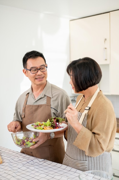 素敵なアジア人夫婦がキッチンで一緒に料理した後食べ物を楽しんでいます