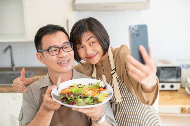 A lovely Asian couple taking pictures or selfies with their food in the kitchen together