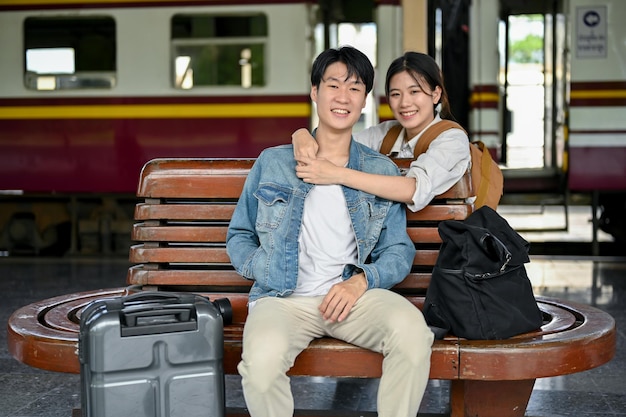 사랑스러운 아시아 여성이 기차역 벤치에서 쉬면서 사랑하는 남자친구를 안고 있습니다.