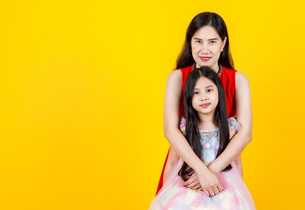 Lovely Asian mother cherish young cute daughter as sweetheart by kindly hug from back with warm family love and empathy care of child girl, together smile for isolated portrait of happy female couple