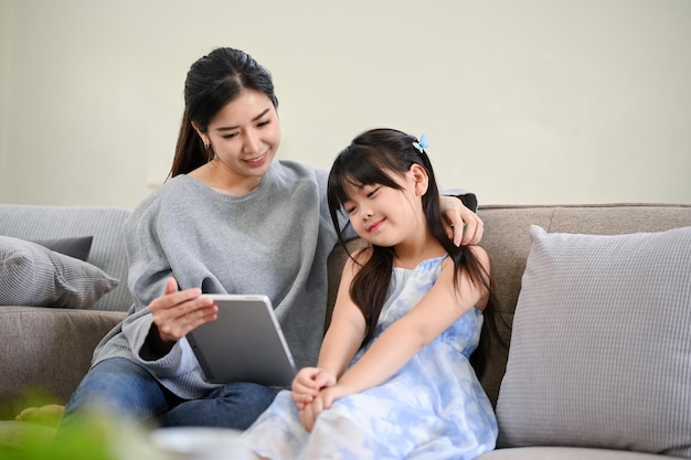 A lovely Asian mother watches a kid's cartoon on a tablet with her young daughter