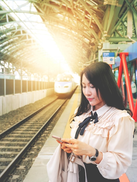 A lovely Asian woman stand playing with a smartphone while waiting for the highspeed train