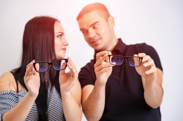 Lovely attractive couple sitting together and looking at each\
other holding glasses in hands young couple showing eyeglasses in\
black frame sitting on white background