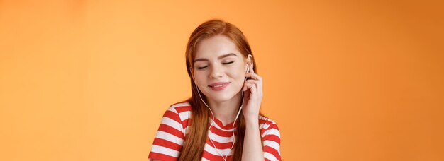 Lovely attractive redhead caucasian s woman listen music close eyes tender smile touch earphone ear