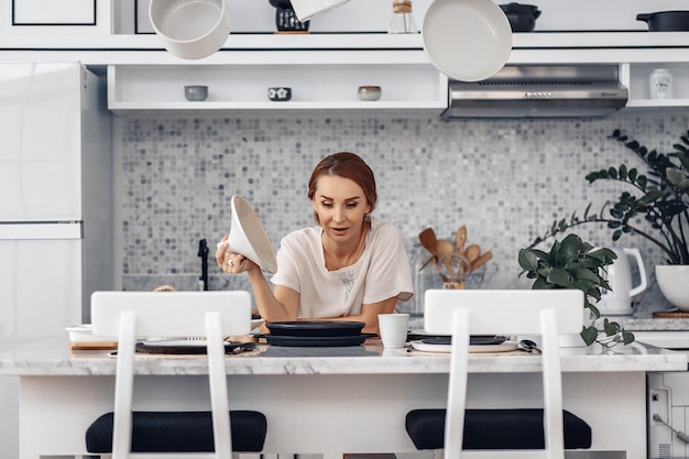 Lovely beautiful adult housewife cooking on the stove in her white light kitchen and opening the lid of a frying pan. Delicious food concept