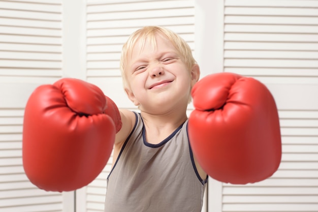 Photo lovely blond boy in red boxing gloves. sports