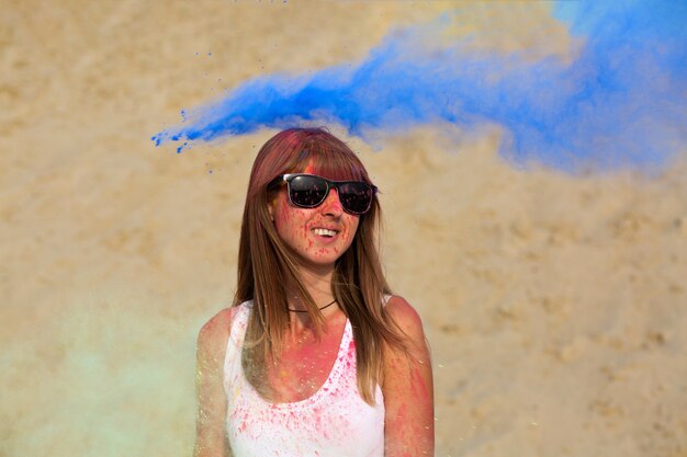 Прекрасная блондинка в солнцезащитных очках играет с синей краской Холи в пустыне