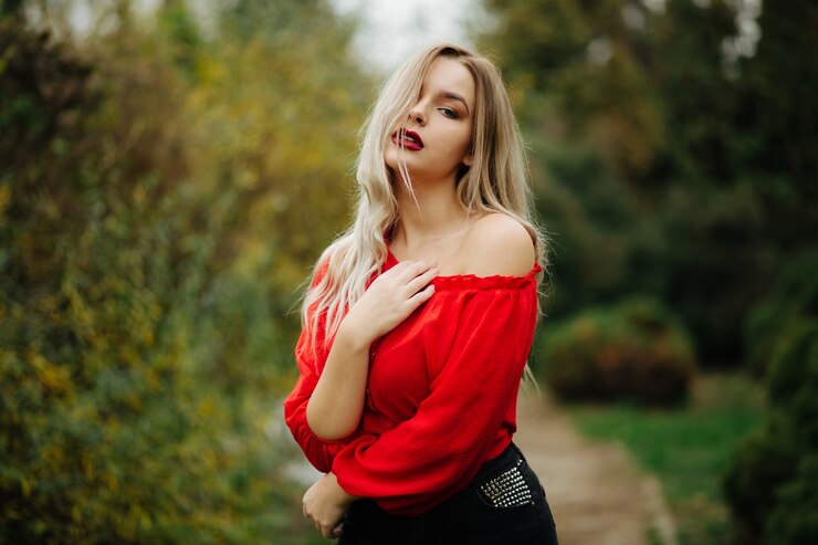 Photo lovely blonde woman in red blouse posing with naked shoulder at the thuja trees