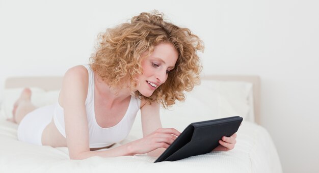 Lovely blonde woman relaxing with her tablet while lying on a bed