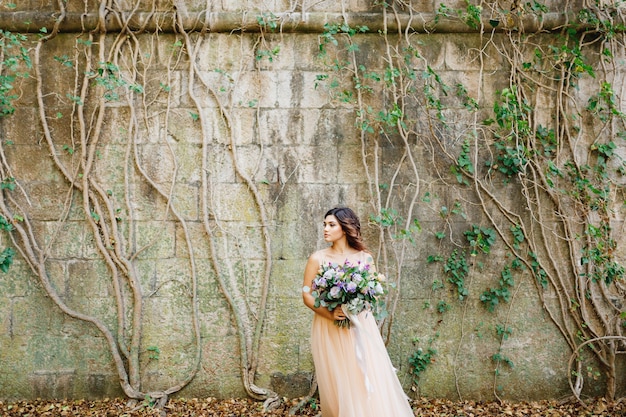 Bella sposa in un abito da sposa beige con un bel mazzo di fiori