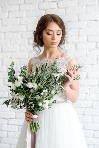 Lovely bride with bouquet of flowers. brunette on a fawn white brick wall