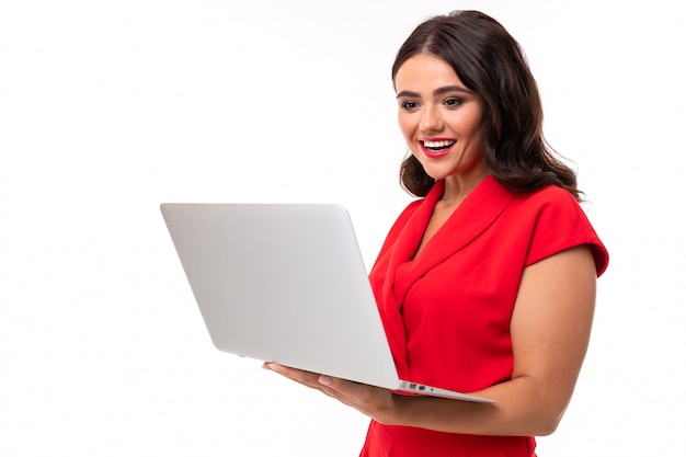 Lovely brunette girl in red dress holding a laptop in her hands on white