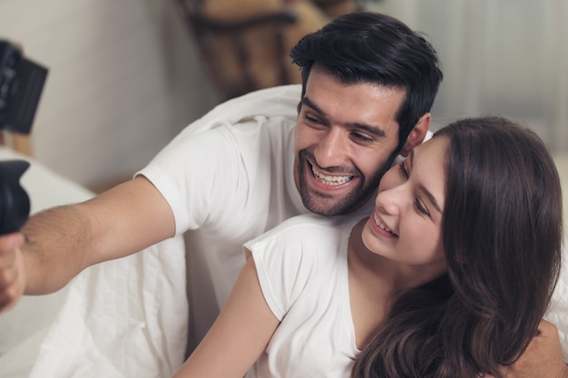 Lovely caucasian couple lying in bed and smile while doing a selfie using a mobile phone
