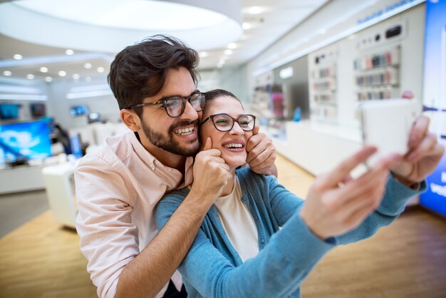 店の電話でselfieを取るハイテクストアの素敵な陽気な流行に敏感な多民族のカップル。