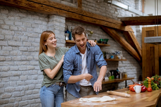 Lovely cheerful young couple preparing dinner together and having fun at rustic kitchen