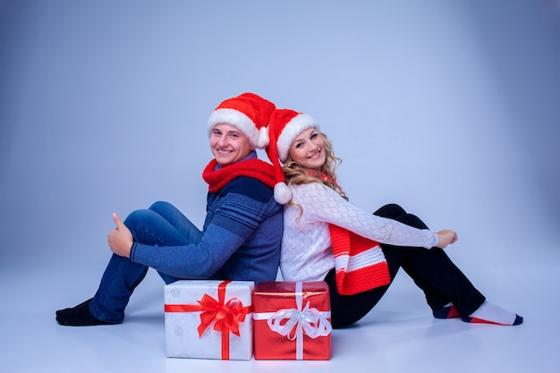 Прекрасная рождественская пара в шляпах Санта-Клауса, сидя с подарками на синем