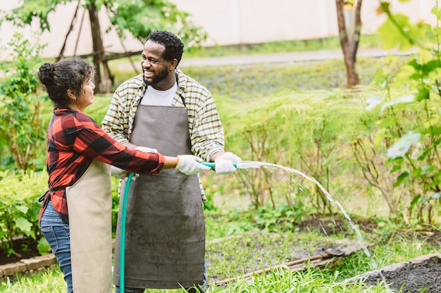 Bella coppia uomo nero con moglie persone pianta di irrigazione nel giardino sorridendo felice insieme