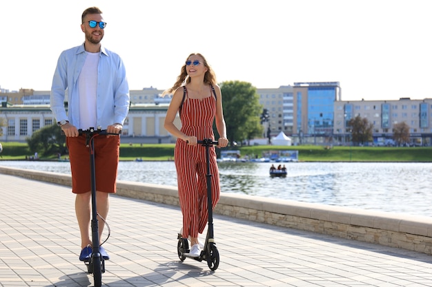 Lovely couple having fun driving electric scooter along the city promenade.