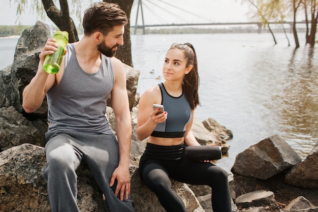 Lovely couple is sitting together near a lake shore and looking to each other