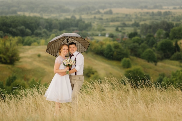 Lovely couple of newlyweds holding an umbrella in their hands against beautiful views of green nature