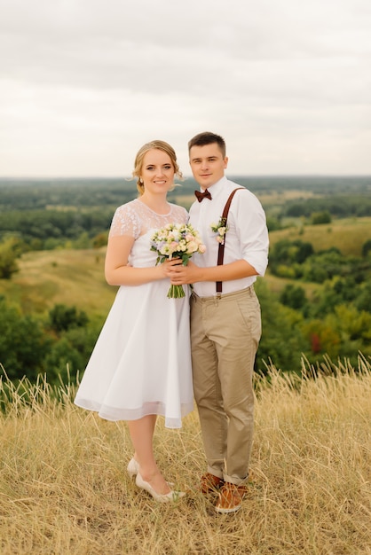 Lovely couple of newlyweds posing against beautiful views of green nature. Pre-wedding photoshoot