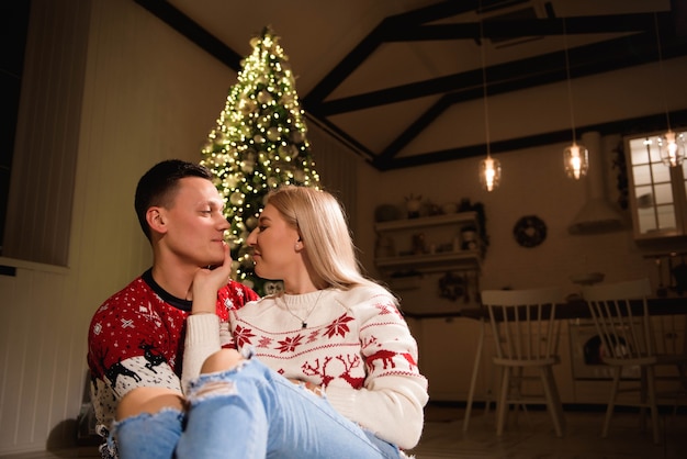 크리스마스 스웨터를 입고 포옹하는 카펫에 앉아 있는 사랑스러운 커플.