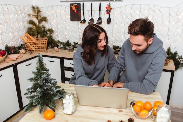 사랑스러운 부부는 부엌에 앉아 노트북을 사용하여 인터넷 화환 가정의 아늑한 인테리어에서 선물을 구입합니다.