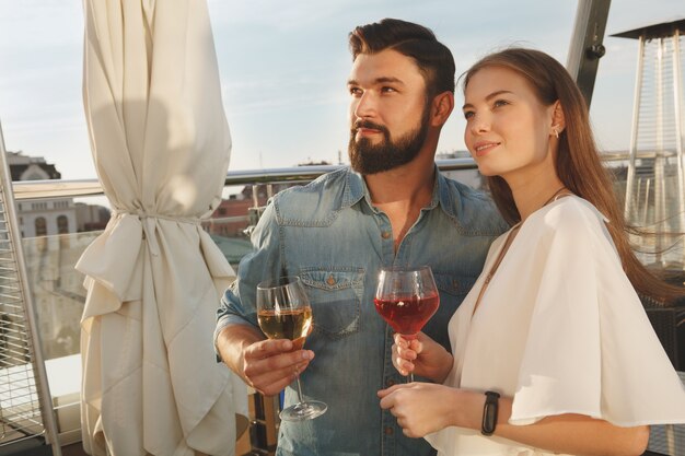 Lovely couple smiling, looking away joyfully while drinking wine on bar terrace