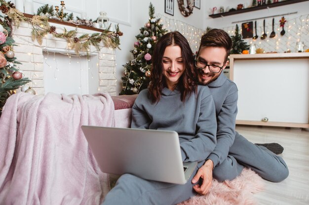 Le coppie adorabili usano il computer portatile acquista i regali presenti nell'interno accogliente della casa delle ghirlande di internet