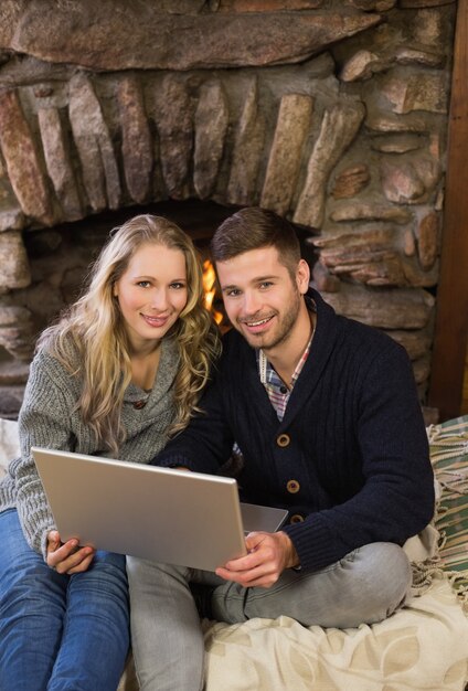 Lovely couple using laptop in front of lit fireplace