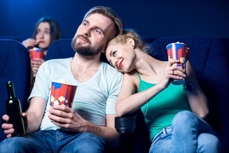 Photo lovely couple watching film sitting together with popcorn in the cinema
