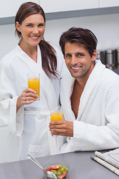 素敵なカップルのバスローブを着て、オレンジジュースのガラスを保持