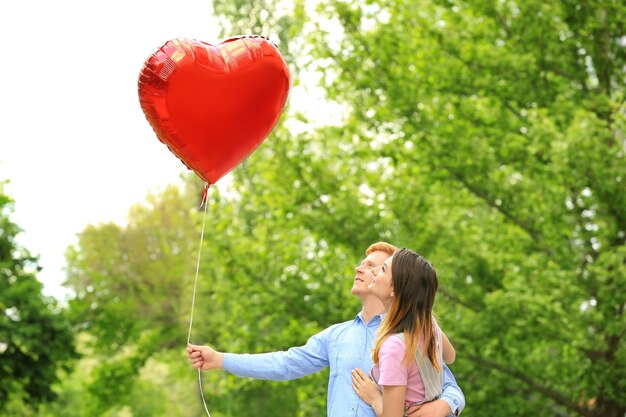 Прекрасная пара с воздушным шаром в форме сердца в парке в солнечный день