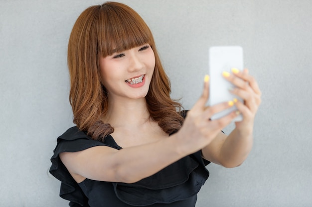 Lovely cute Asian girl making selfie photo with smartphone with happy face, concept for teen and modern people lifestyle with technology.