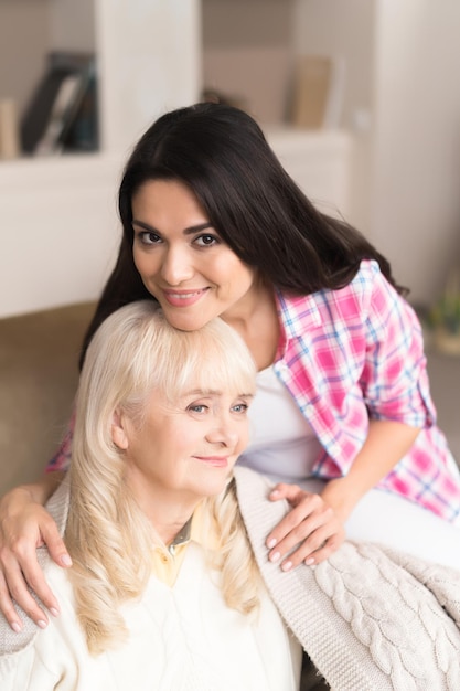 Lovely Daughter Hugs Her Elderly Mother And Looks With A Smile At Camera. Family Portrait.