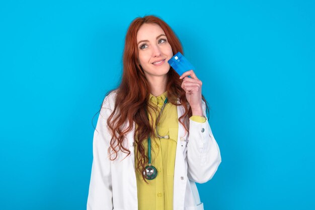 Lovely doctor woman showing credit card and looking away at copy space Pensive