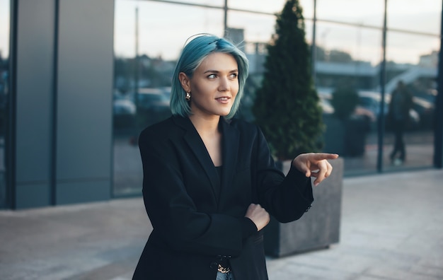 Lovely entrepreneur with blue hair pointing to something while wearing a suit outside