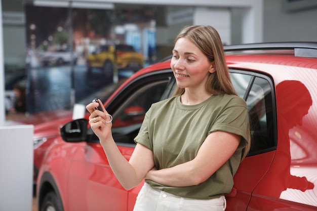 Lovely female driver holding car keys after buying new auto at car dealership