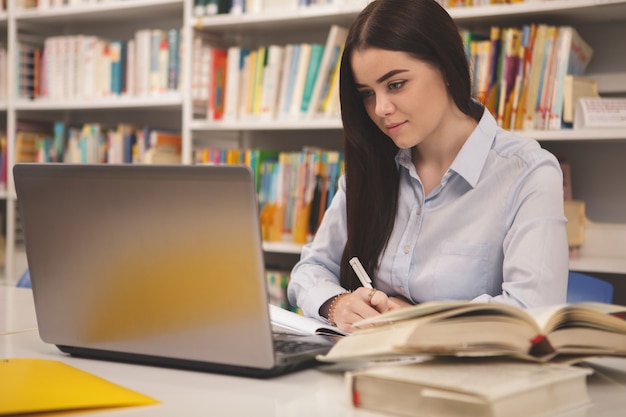 Studentessa adorabile che lavora al computer portatile alla biblioteca