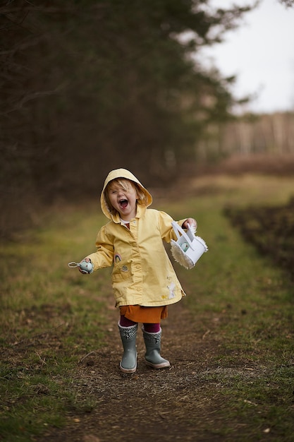 Adorabile e divertente bambina olandese con un cappotto impermeabile giallo e stivali che gioca nel campo di campagna