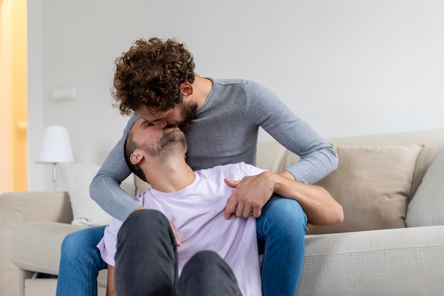 Lovely gay couple kissing while sitting in their living room at home Two romantic young male lovers having fun indoors Young gay couple living together