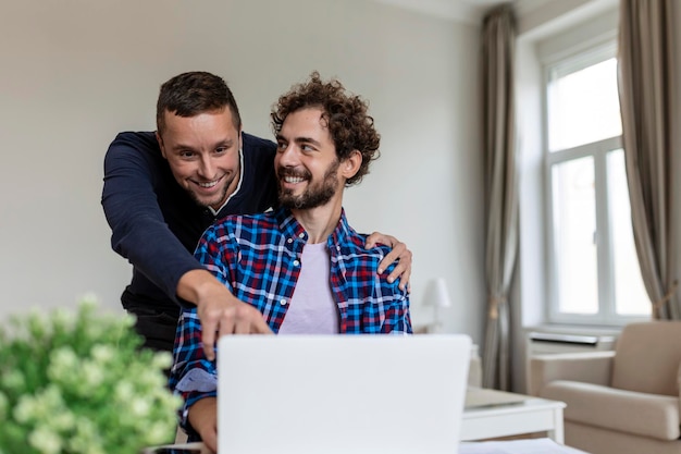 Lovely gay couple laughing together while sitting in their\
living room at home two romantic young male lovers having fun\
surfing the internet indoors young gay couple living together